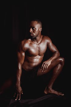 Dark and dynamic portrait of a muscular man posing shirtless on a black background.