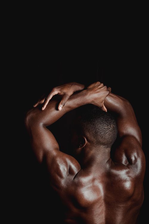 Free A muscular man flexing his back and arms against a dark background. Stock Photo