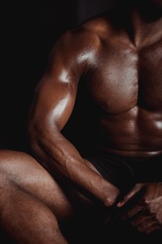 Close-up of a muscular African American man's torso in low light, showcasing strength and athleticism.