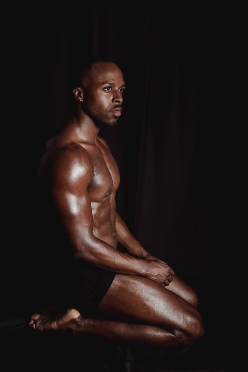 Free A muscular black man kneeling shirtless in a thoughtful pose against a dark background. Stock Photo