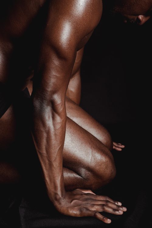 Free Close-up of a muscular African American man kneeling shirtless in dramatic lighting. Stock Photo