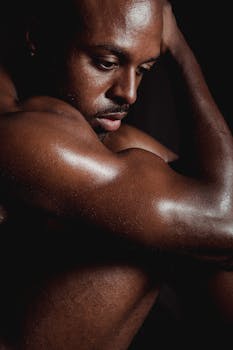 A powerful portrait of a shirtless man showcasing his muscular bicep in dramatic lighting.