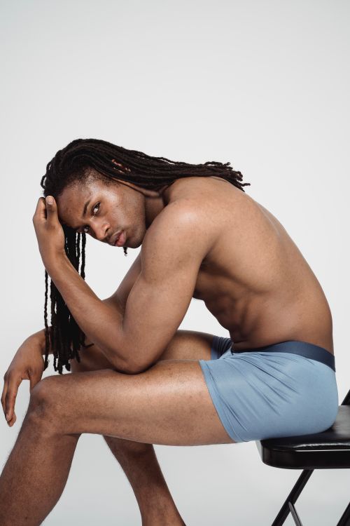 Free A muscular black man with braided hair sitting shirtless on a chair, showcasing fitness. Stock Photo