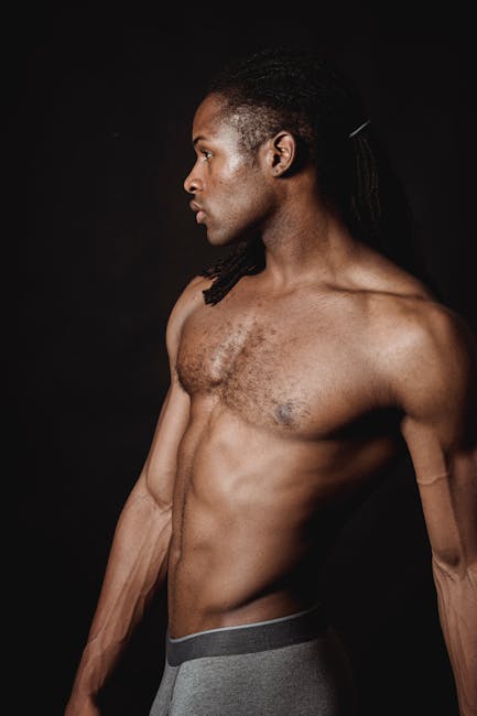 Side profile of a fit, shirtless man showcasing muscles against a dark backdrop.