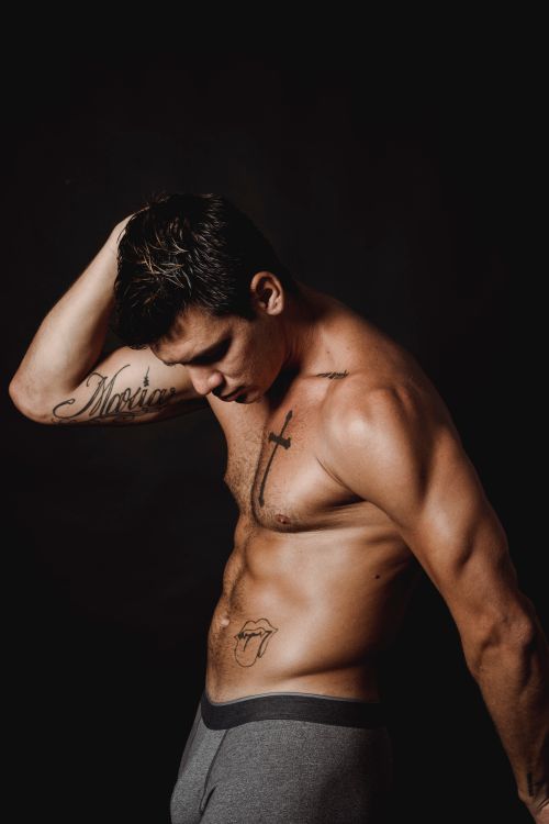 Free Athletic man posing shirtless against dark background, showcasing tattoos and muscles. Stock Photo