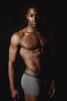 A muscular man posing shirtless against a dark background, showcasing fitness and strength.