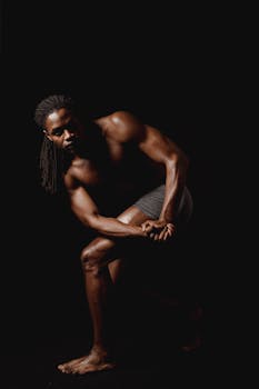 Muscular man posing shirtless in a studio setting highlighting strength and fitness.