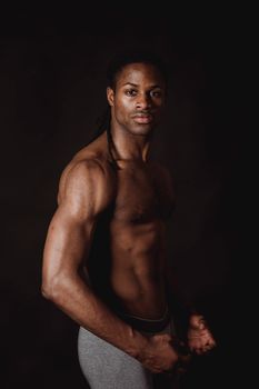 Portrait of a muscular black man posing shirtless against a dark background.