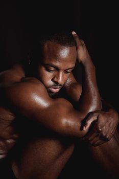 Dramatic photograph of a shirtless, muscular man in a thoughtful pose with a dark background.