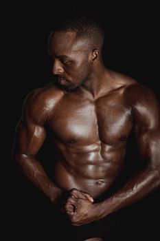 Black athletic man showcasing abs and musculature against a dark backdrop.