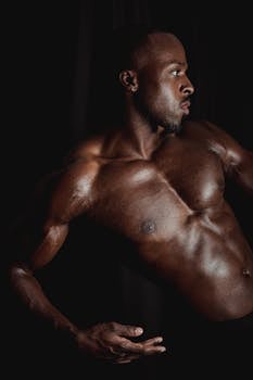 Muscular black man in a strong side profile pose, showcasing defined muscles and strength.
