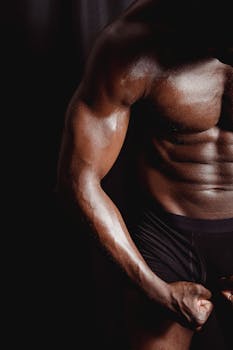 Close-up of a muscular man flexing his arm, highlighting defined muscles against a dark background.