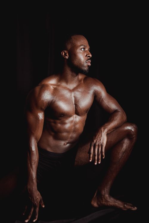Free Strong, shirtless male posing confidently in a low light studio showcasing defined muscles. Stock Photo