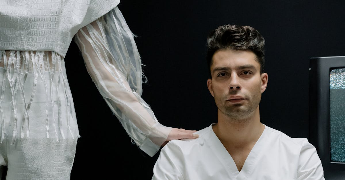 Photo by cottonbro studio A man sits in white attire while a woman in futuristic clothing stands beside in a modern medical setting.