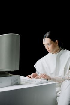 Woman in futuristic attire engaging with a vintage computer in a studio setting.