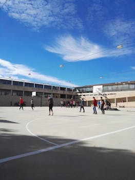 People playing basketball on an outdoor court under a blue sky.