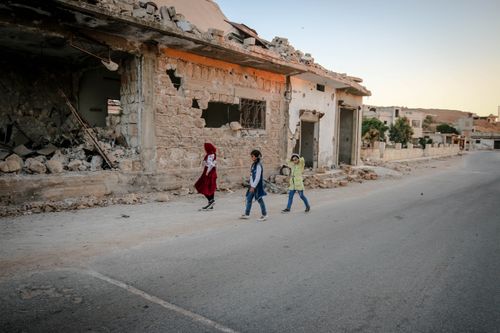 Free Three children walking past a damaged building in Idlib, Syria during the day. Stock Photo