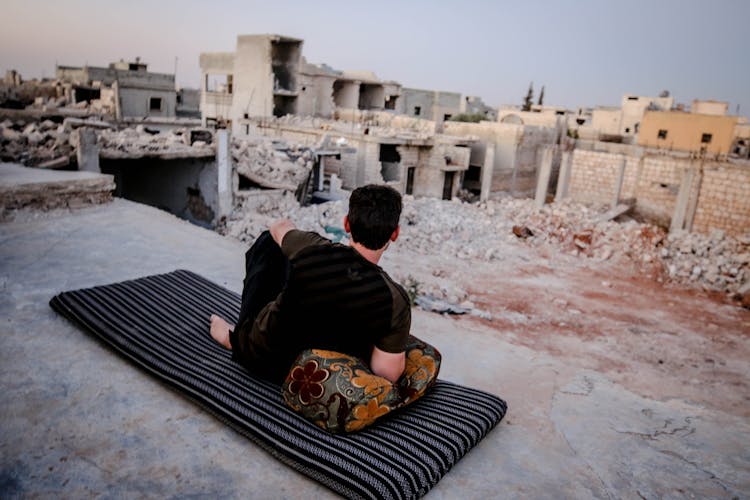 Man Sitting On Carpet Looking At Old City Ruins