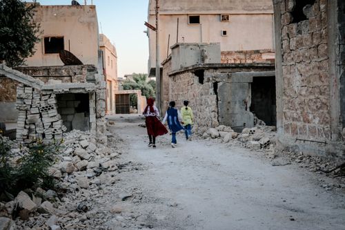Free Children walk through the ruins of Idlib, Syria, showcasing resilience amidst destruction. Stock Photo