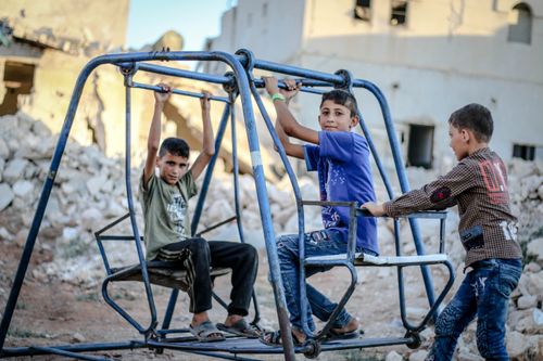 Free Children enjoying a swing amidst rubble in Idlib, Syria, showcasing resilience. Stock Photo