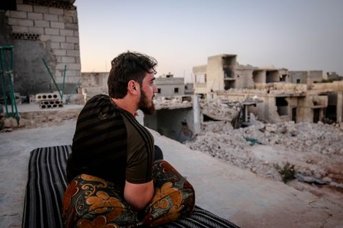 Free A man in Idlib, Syria, sits thoughtfully amidst the ruins of buildings, reflecting the impact of conflict. Stock Photo