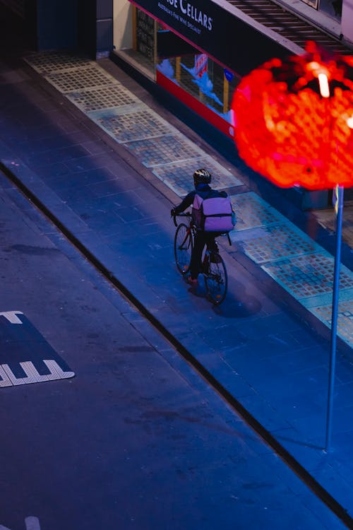 Free A Person with a Bag Riding a Bicycle on a Sidewalk Stock Photo