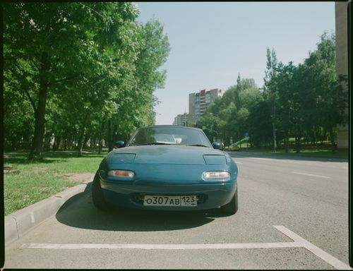 Free Classic blue car parked on a sunny urban street with lush trees. Stock Photo