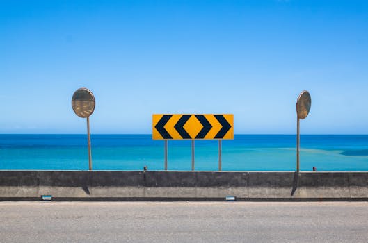 Coastal road with yellow chevron traffic sign and blue ocean horizon.