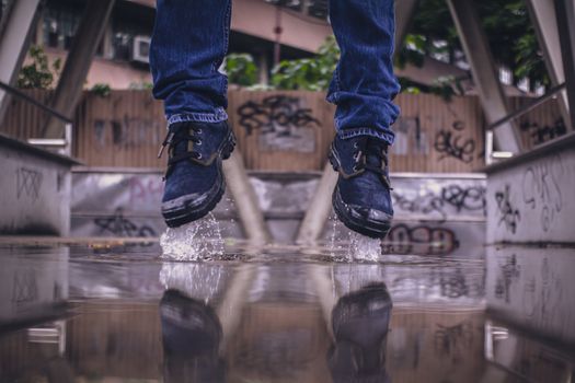 Close-up of boot-clad feet splashing in a puddle with urban graffiti background.