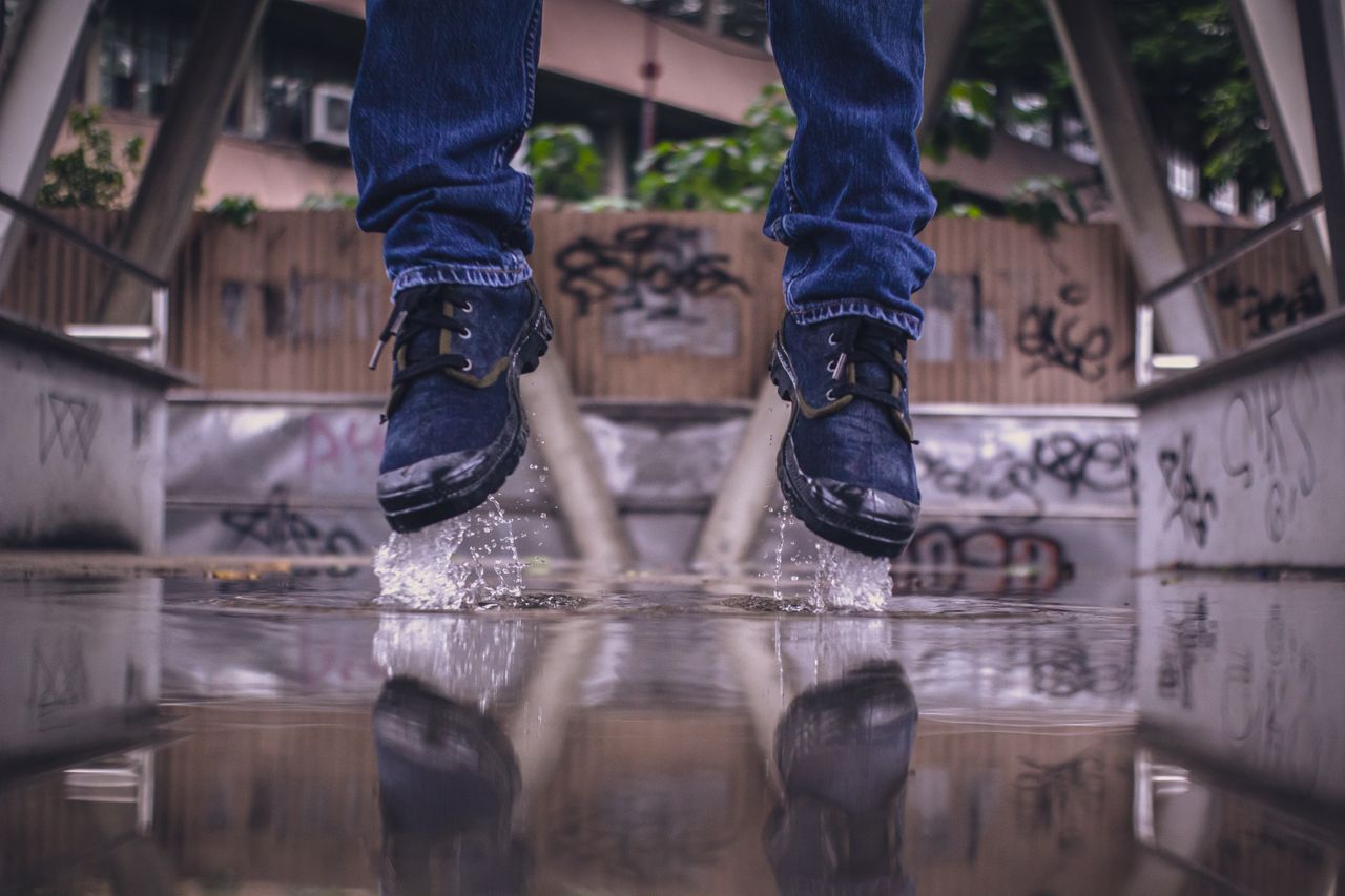 close up of boot clad feet splashing in a puddle with urban graffiti b