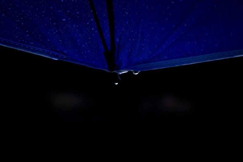 A focused shot of a blue umbrella with water droplets in a dark setting, conveying a rainy mood.