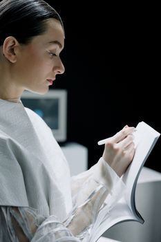 A scientist in a futuristic laboratory takes notes in a notebook.