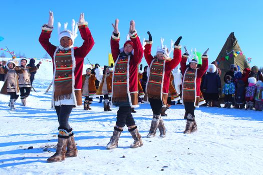 Dancers in traditional attire perform in snowy landscape, celebrating winter culture.