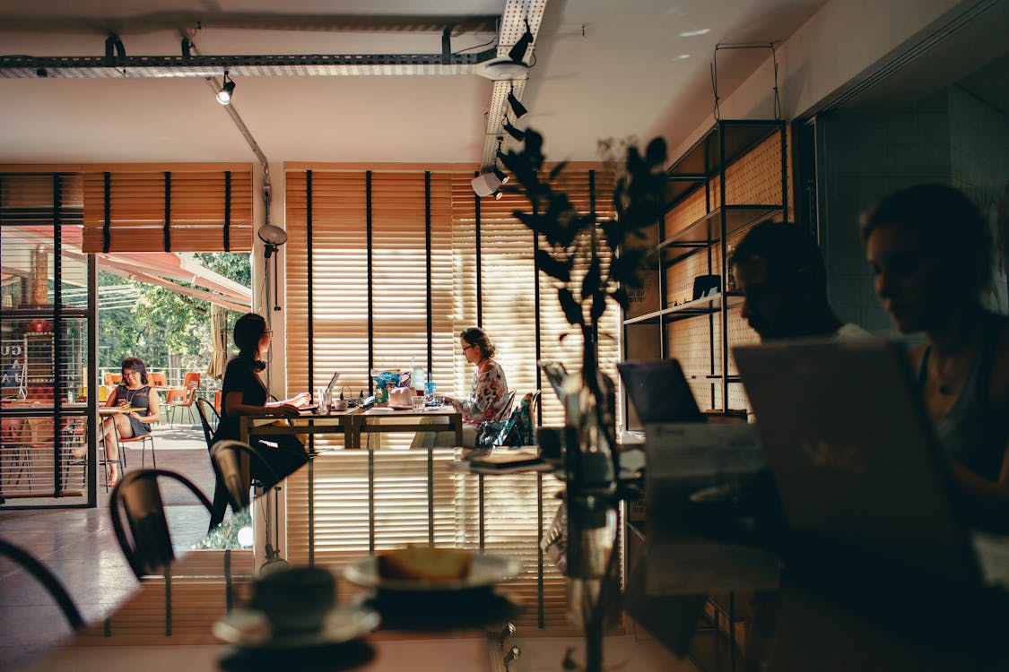 Free Interior of a bustling café with people working on laptops, creating a modern, collaborative atmosphere. Stock Photo