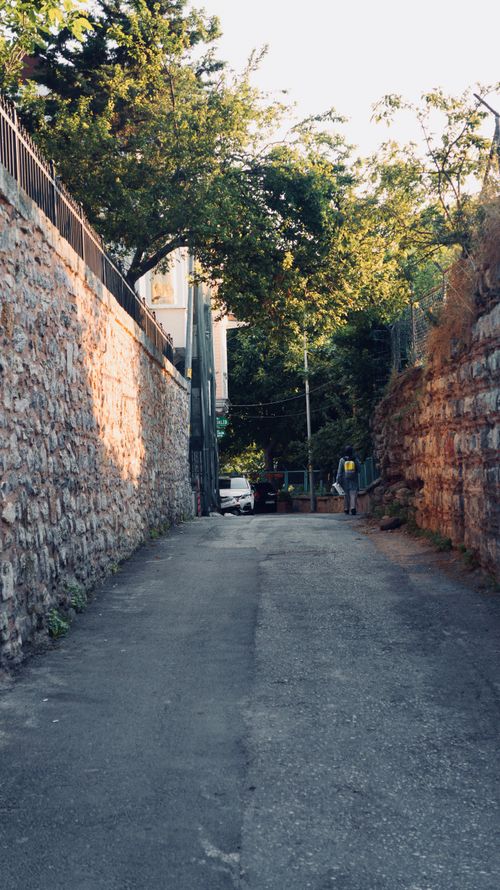 Free A quiet alley in Istanbul flanked by stone walls and trees, captured in the gentle light of day. Stock Photo