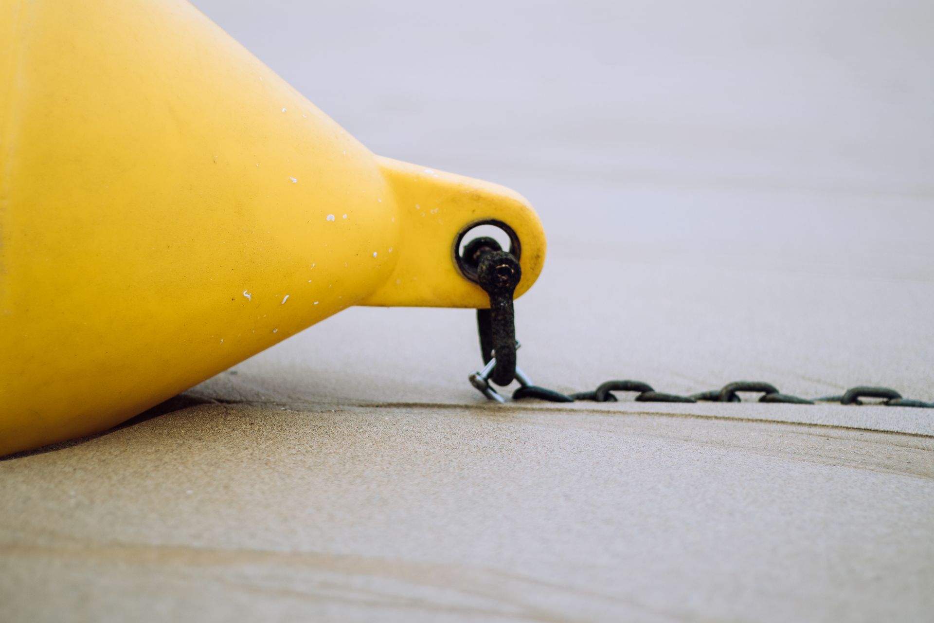 Close-up of a yellow buoy tethered with a chain on a sandy beach, displaying texture and weathering.