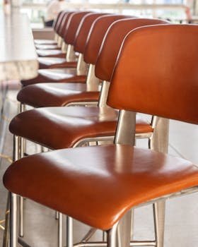 Stylish brown leather bar chairs lined up indoors, perfect for modern dining spaces.