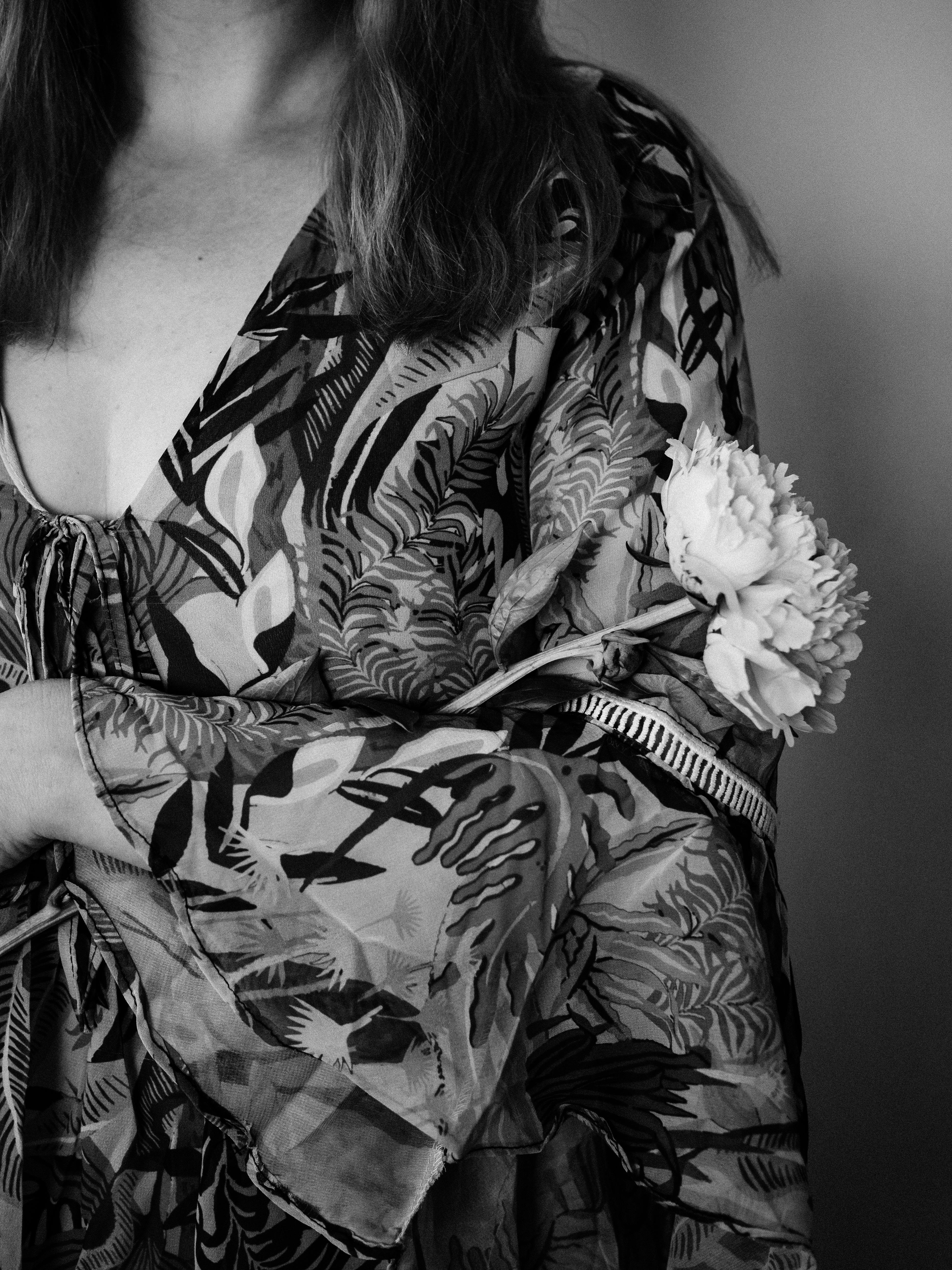 A woman in a patterned dress gently holds a peony, captured in a grayscale portrait.