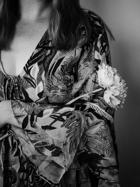 A woman in a patterned dress gently holds a peony, captured in a grayscale portrait.