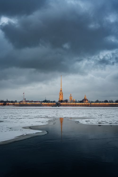 Free Dramatic winter landscape of a city with a frozen river and overcast clouds, ideal for mobile wallpaper. Stock Photo