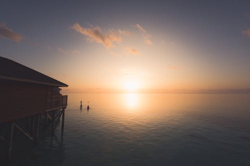 Fotografi Siluet Orang Di Perairan Dengan Latar Belakang Matahari Terbenam