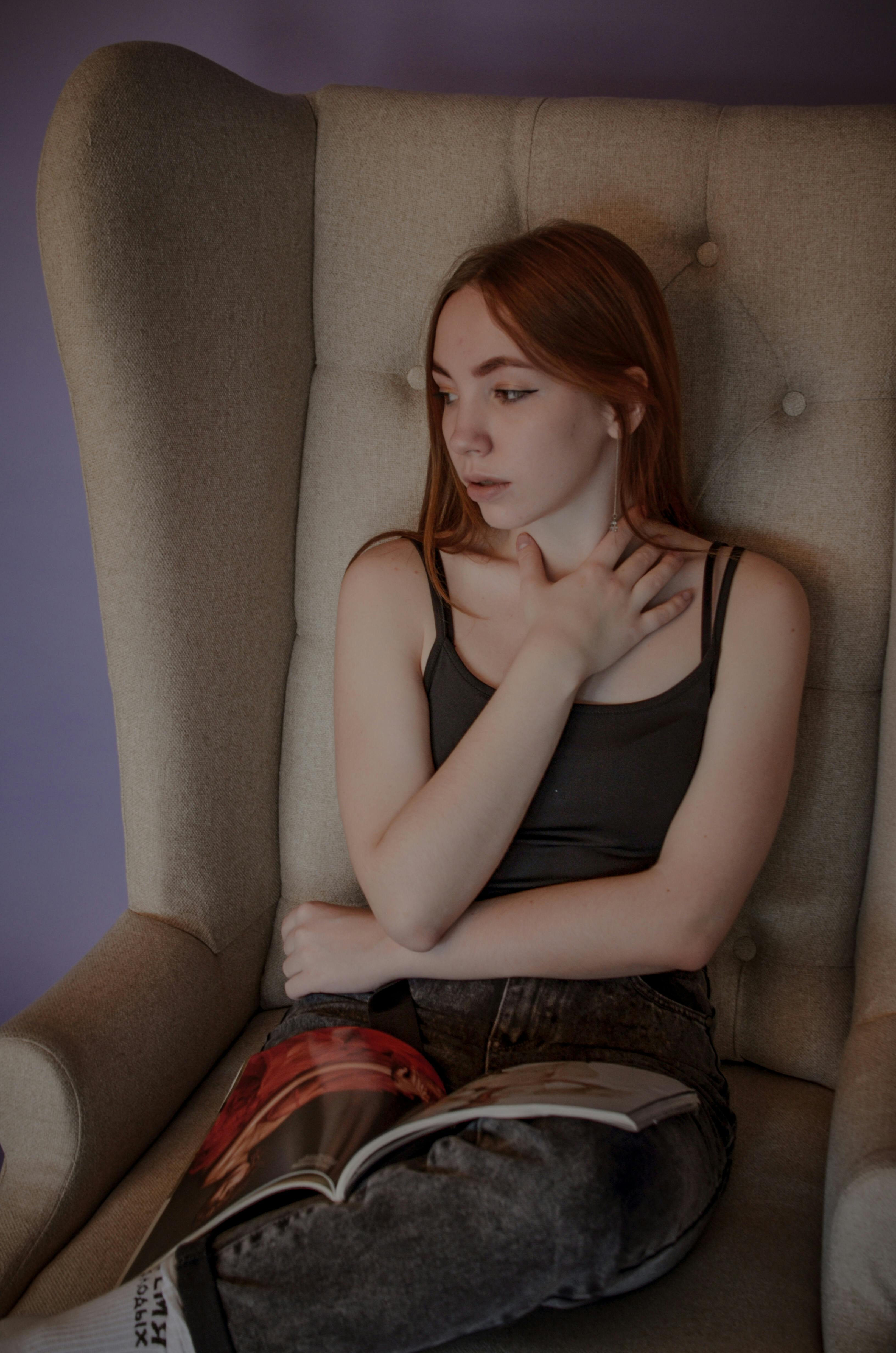 young woman in black tank top sitting on an armchair with a magazine on lap