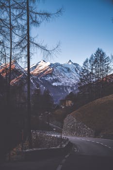在晴朗的冬日天空下，风景如画的山路通往白雪覆盖的山峰