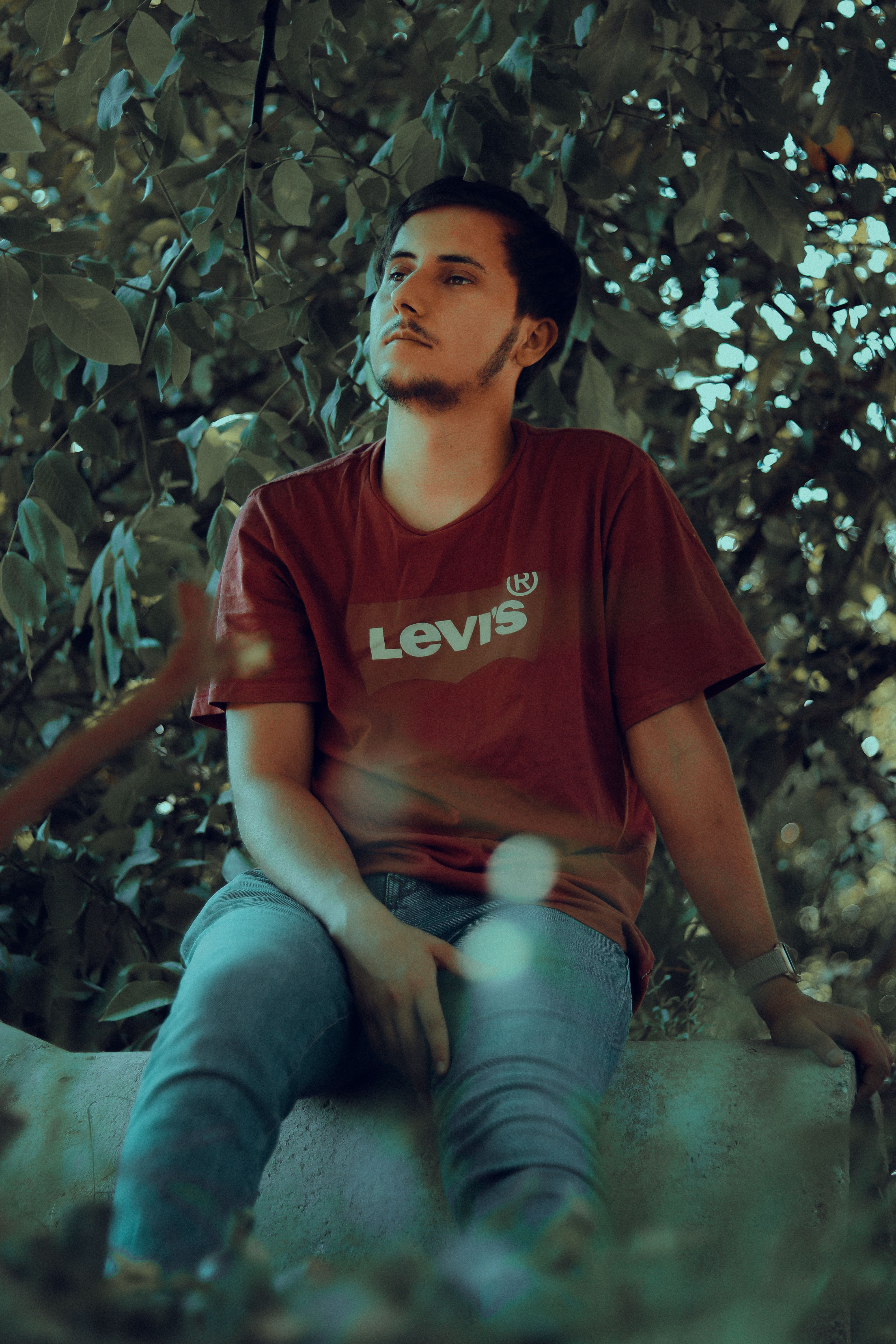 Casual young man in denim enjoying a peaceful outdoor moment under leafy trees.