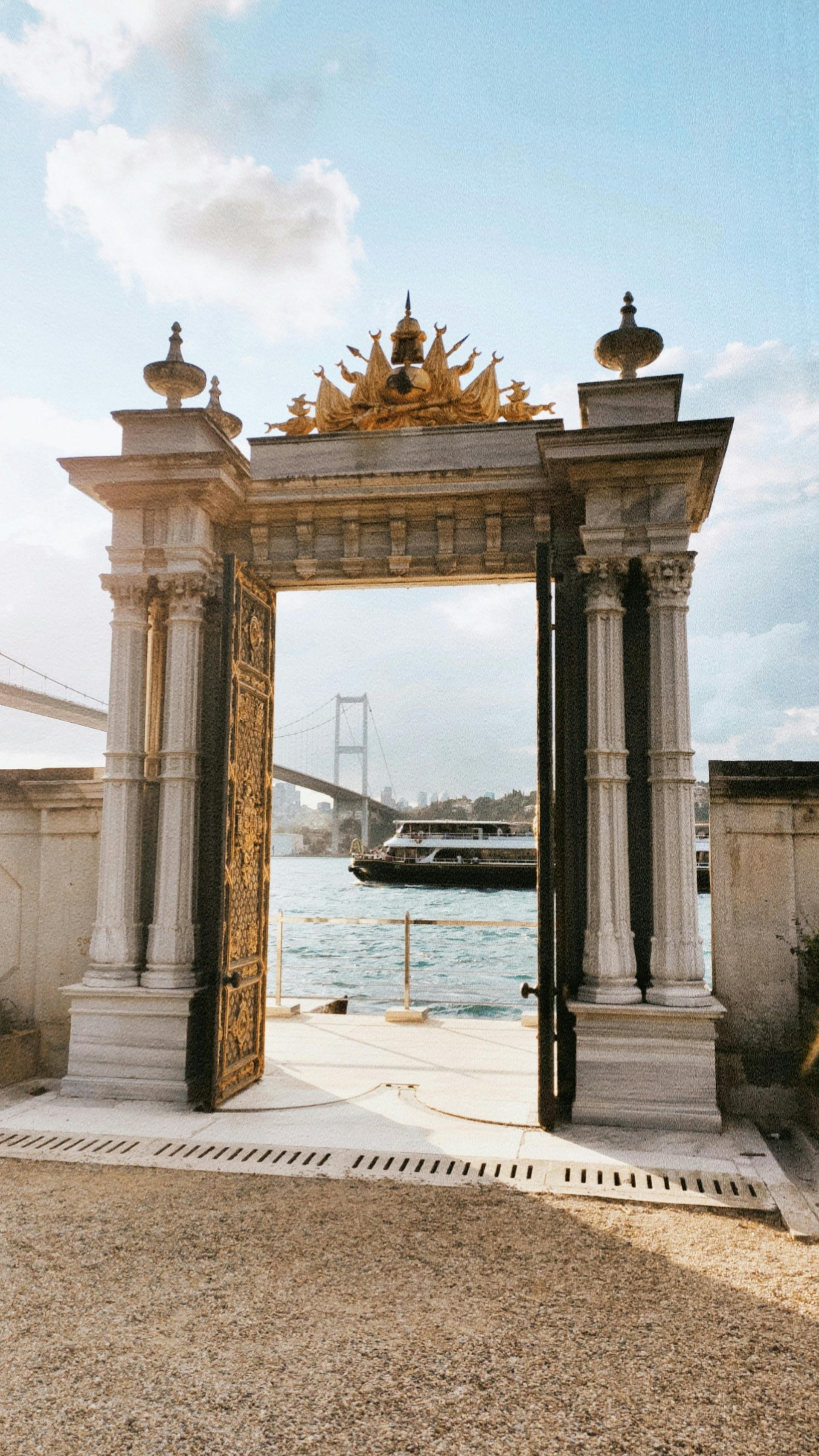 Elegant stone archway overlooking the Bosphorus with a boat and bridge in Istanbul's scenic setting.