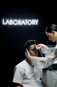 A scientist examines a patient in a sterile laboratory with a neon sign overhead.