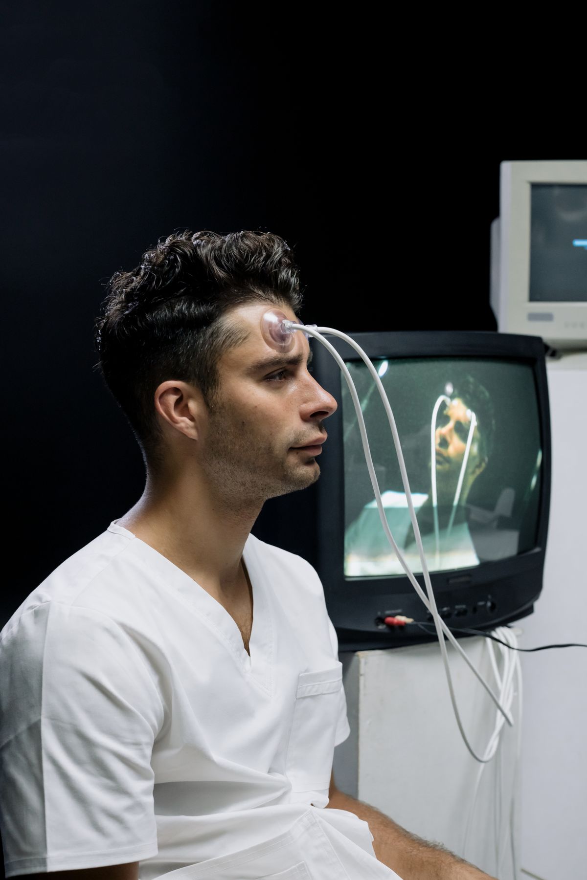 A person with recording sensors attached, seated beside a monitor displaying activity.