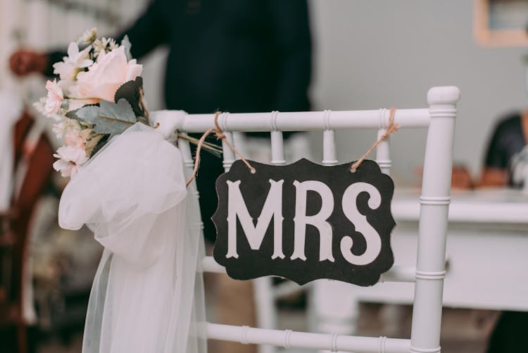 A Black And White Mrs Sign Hanging On A White Wooden Chair With Veil And Flowers