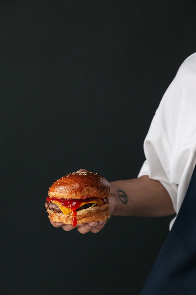 Photo Of A Person's Hand Holding A Burger With Red Sauce