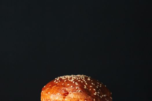 Close-up of a delicious sesame seed burger bun against a dark backdrop, perfect for food photography.